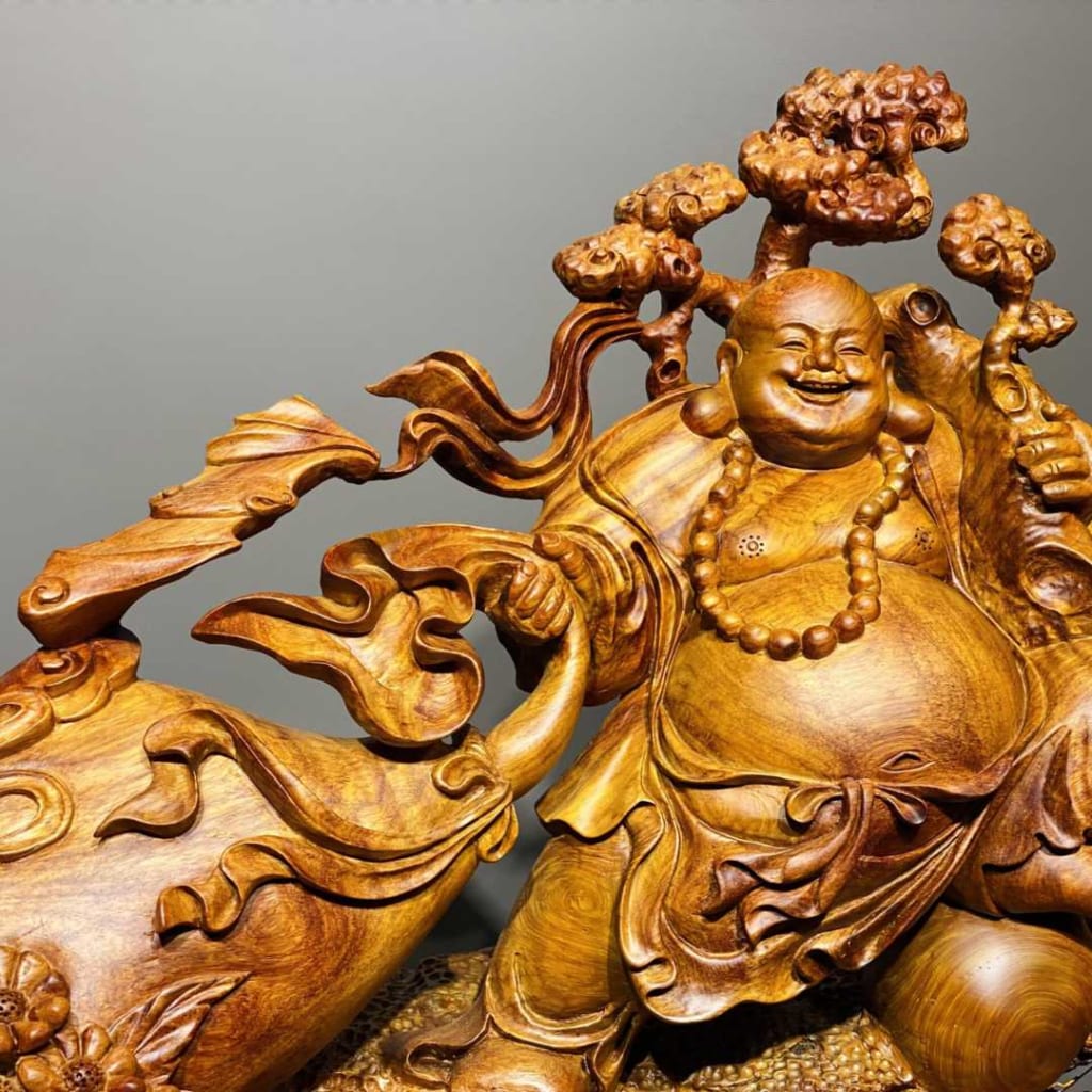 Tượng Phật Di Lặc gỗ màu nâu, tay bên phải kéo một bao tiền, tay bên trái có một cái cây