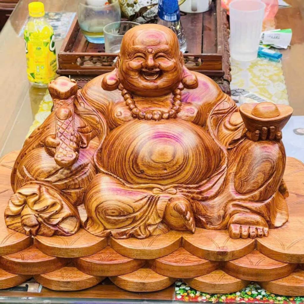 Phật Di Lặc ngồi trên một cái đế được xếp từ rất nhiều đồng tiền xu. Tay phải cụ cầm một cây gậy như ý, cây trái cụ cầm một thỏi vàng
