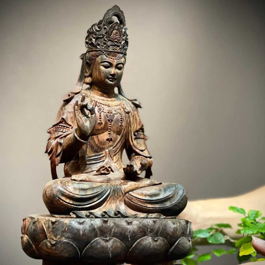 Tượng Phật Quan Âm gỗ trắc có màu đỏ nâu và xanh xen kẽ. Ngài vắt hai chân với nhau, tay phải bắt ấn, đầu búi tóc và có khắc hình người đang niệm Phật. Ở bên cạnh bức tượng có một cái cây xanh nhỏ