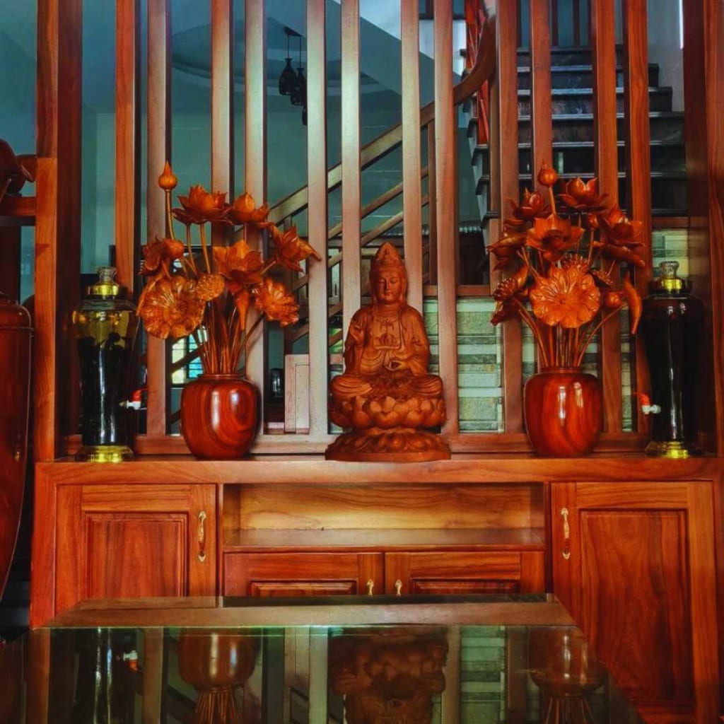 Tượng Phật gỗ được đặt trên một cái bàn gỗ. Bên trái và bên phải ngài có hai lọ hoa bằng gỗ. Đằng sau Ngài là những thanh gỗ dọc