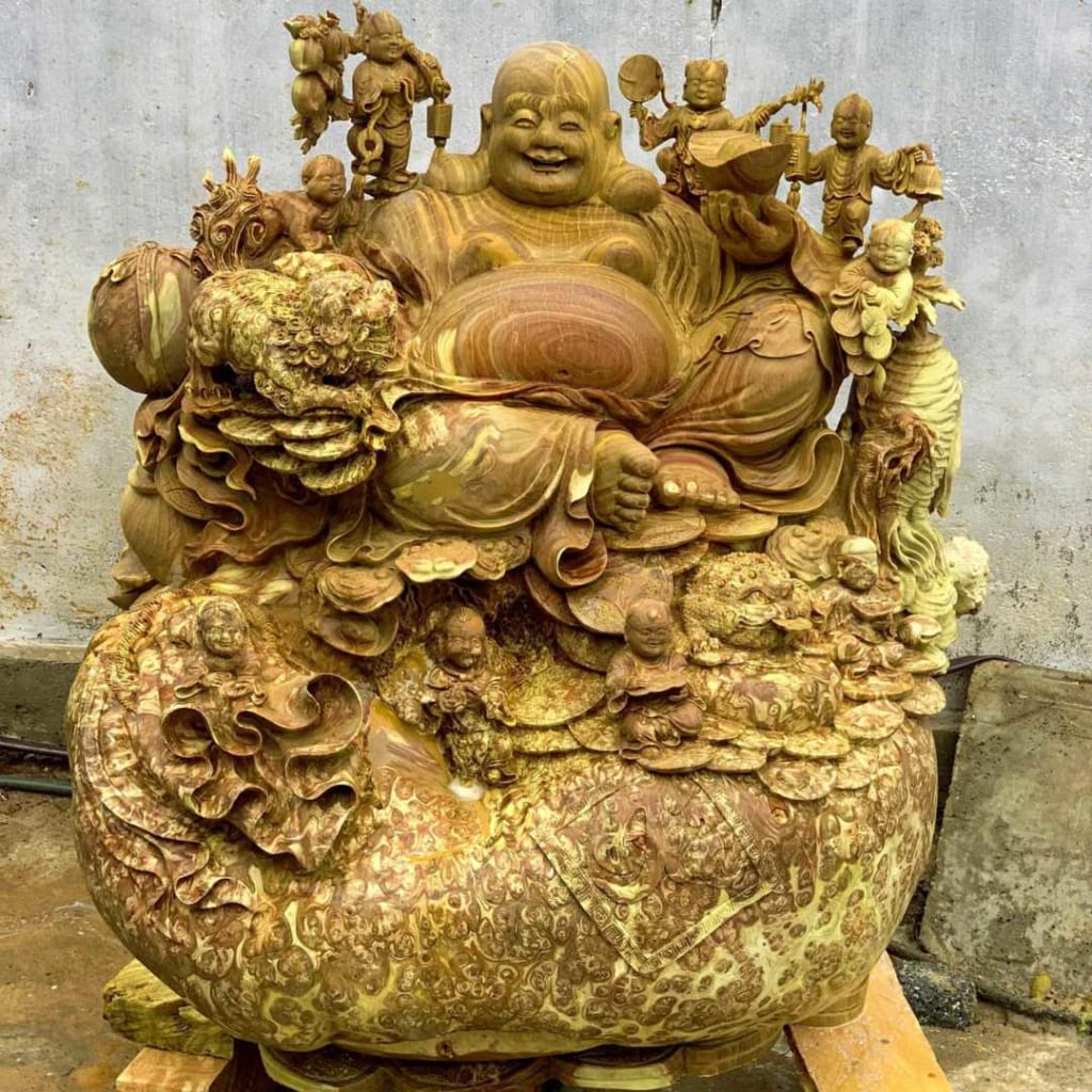 tượng Phật Di Lặc bằng gỗ, hở bụng, tay cầm thỏi vàng. cụ Di Lặc ngồi trên một khúc thân cây gỗ rất to.